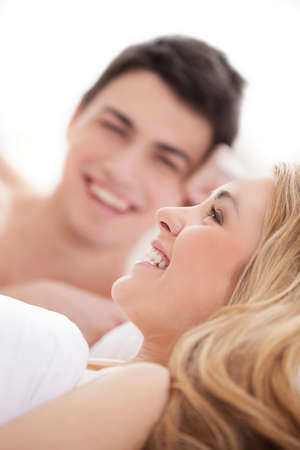 Loving couple in bed. Cheerful young loving couple lying on bed and smilingの写真素材