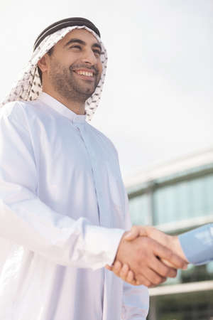 Business partners shaking hands. Low angle view of Arab businessman shaking someone hand and smilingの写真素材