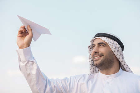 Arab businessman with paper airplane. Cheerful Arab businessman holding an airplane and looking awayの写真素材