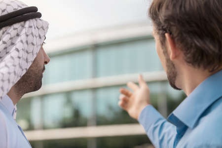 Discussing business issues. Rear view of two business partners discussing something while one of...
