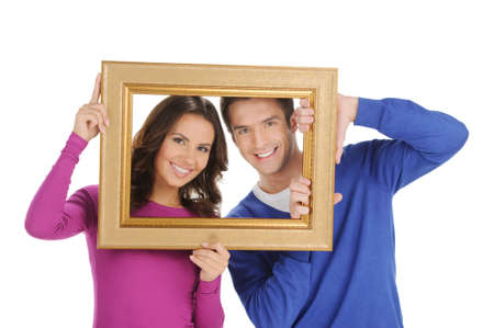 Couple in frame. Beautiful young couple looking through a picture frame and smiling while isolated on whiteの写真素材