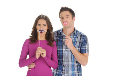 Couple grimacing. Beautiful young couple holding the fake moustache and lips on stick  while isolated on whiteの写真素材