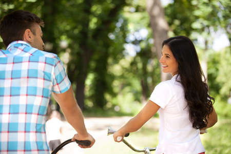 Riding bikes. Rear view of cheerful young couple riding bikes in parkの写真素材