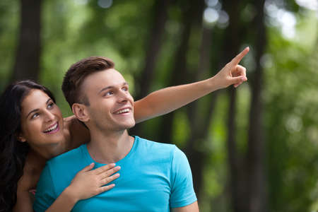Couple having fun in park. Young loving couple having gun at park while woman pointing away with fingerの写真素材