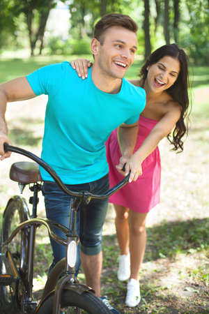 Couple in spring park. Cheerful young couple with bicycle having fun in parkの写真素材