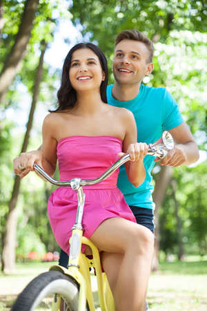 Young couple biking. Cheerful young loving couple riding bike in parkの写真素材