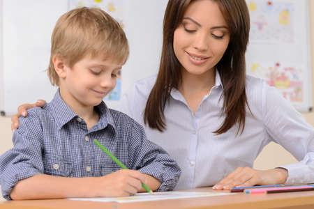 Teacher with pupil. Confident schoolboy writing something in note pad while sitting near his teacherの写真素材