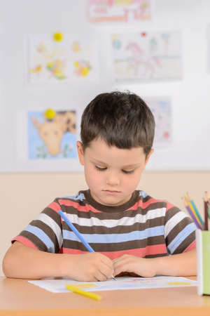 Diligent pupil. Confident schoolboy drawing while sitting in classroomの写真素材