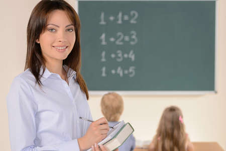 Confident teacher. Cheerful young teacher smiling at camera while pupils studying on backgroundの写真素材