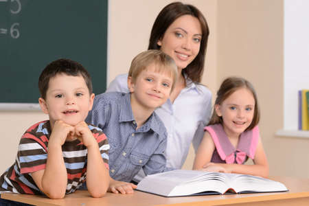 Teacher and pupils. Confident young teacher sitting together with pupils and reading bookの写真素材
