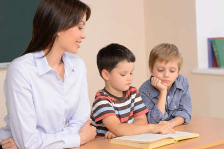 Reading together. Cheerful young female teacher sitting near two schoolboys reading a bookの写真素材