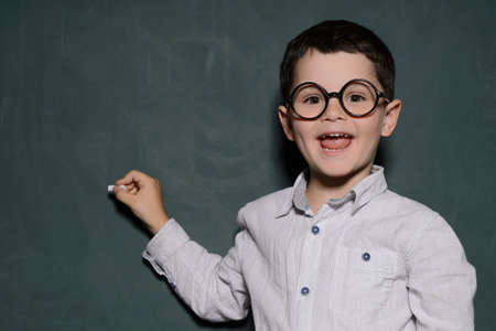 Happy learner. Cheerful little schoolboy in glasses standing near the blackboard and smilingの写真素材