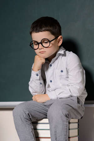 Thoughtful little schoolboy. Little schoolboy sitting on a book stack and holding his hand on chinの写真素材