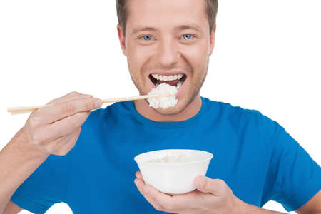 Man eating rice. Portrait of cheerful young man eating rice from the bowl while standing isolated on whiteの写真素材