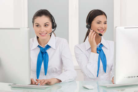 Two customer service representatives at work. Two cheerful young female customer service representatives in headset working at the computer and smilingの写真素材