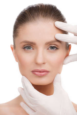 Medical exam. Portrait of beautiful young woman looking at camera while hands in gloves examining her faceの写真素材