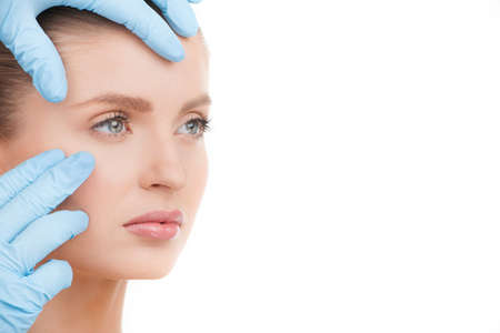 Face examining. Portrait of beautiful young woman looking away while hands in gloves examining her faceの写真素材