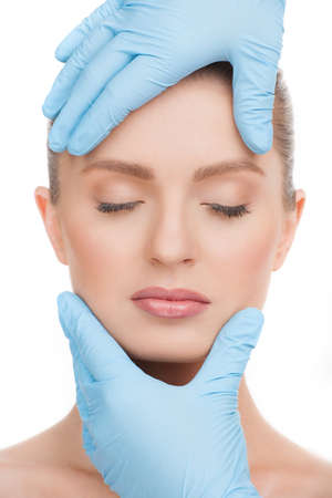 Examining face. Portrait of beautiful young woman with closed eyes and hands in gloves examining her faceの写真素材