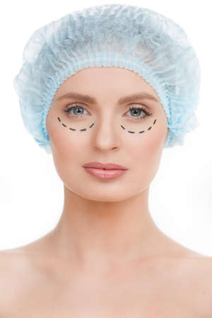 In search of perfection. Portrait of beautiful young woman in medical headwear and markings on face looking at camera while isolated on whiteの写真素材
