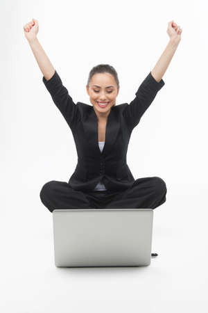Businesswoman with laptop. Cheerful young businesswoman looking at the computer monitor and holding her arms raised while isolated on whiteの写真素材