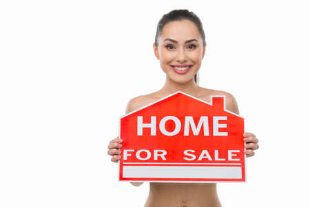 Home for sale. Beautiful naked woman holding a home for sale sign while isolated on whiteの写真素材