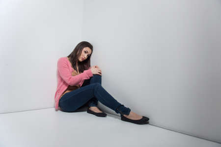 Loneliness. Depressed young woman sitting on the floor and leaning her head at the wallの写真素材
