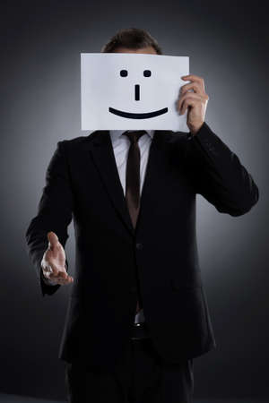 Smiling mask  Businessman holding a poster with smile on it in front of face and stretching out handの写真素材