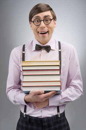 Nerd with book stack. Young nerd man holding a book stack while standing isolated on greyの写真素材