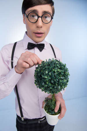 Nerd with plant. Young nerd man holding plant in his hands while isolated on blue