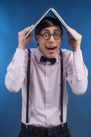 Nerd with book. Young nerd man holding a book on head while standing isolated on blue