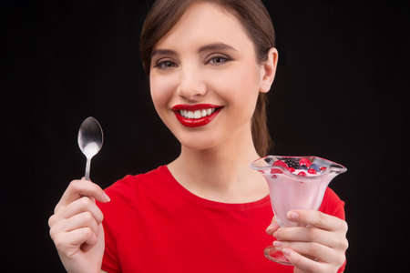 Woman with dessert. Close-up of woman holding berry dessert and spoon while isolated on blackの写真素材