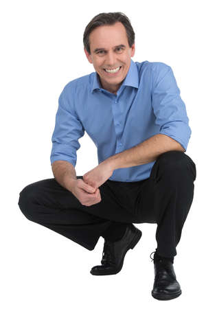 Executive crouching. Cheerful mature businessman sitting crouched and looking at camera while isolated on whiteの写真素材
