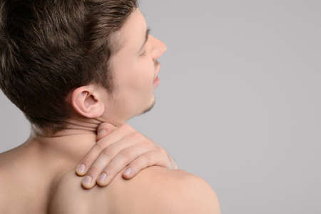 Pain in shoulder. Rear view of young shirtless men touching his shoulder by hand and keeping eyes...