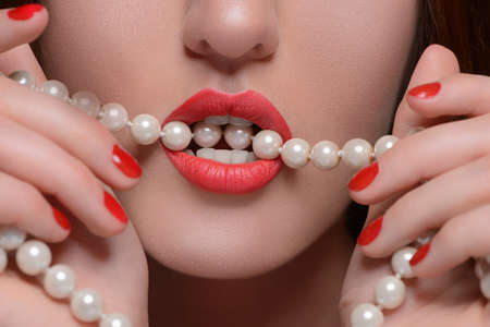Pearl white teeth. Close-up of beautiful women holding pearl necklace in her mouthの写真素材