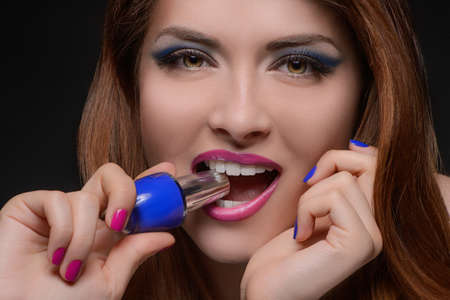I choose the blue one! Portrait of beautiful women holding a nail polish in her teethの写真素材