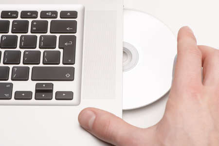 Person sliding a blank CD into a white laptopの写真素材