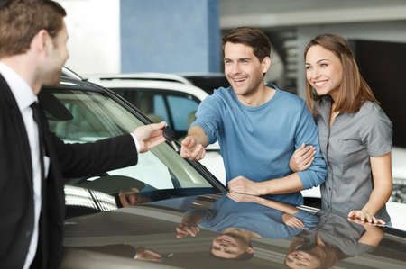 They have made a right vehical choise. Young car salesman giving a key from the new car to the...