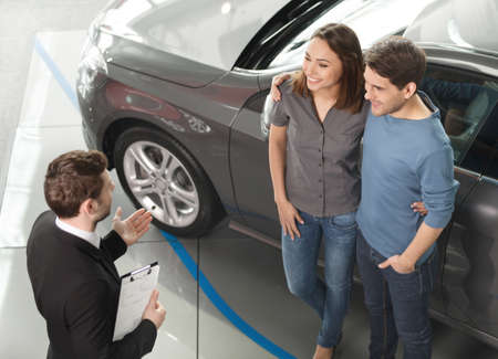 Buying their first car together. High angle view of young car salesman standing at the dealership...
