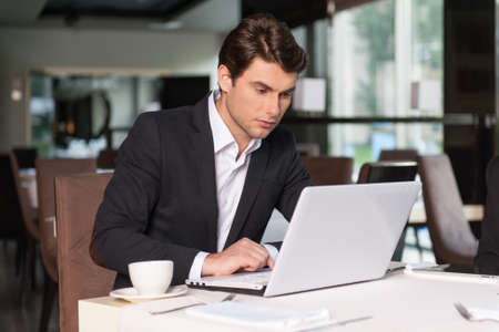 Handsome businessman working with laptop. Sitting at the restaurant and drinking coffee.の写真素材