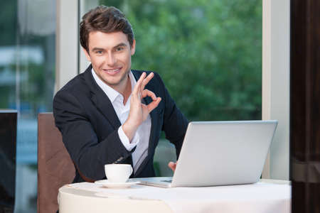 Attractive businessman showing ok sign. Smiling at camera sitting at restaurantの写真素材