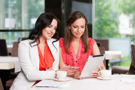Two female friends looking at touchpad. Smiling and looking happyの写真素材