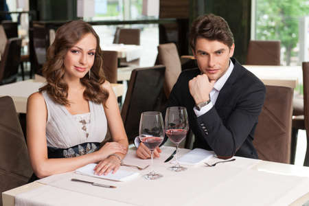 Beautiful couple sitting at the restaurant. Waiting for food, looking at cameraの写真素材