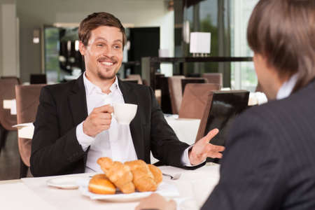 Cheerful smiling funny business man talking to his friend. Drinking coffee with donutsの写真素材