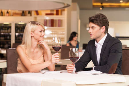 Beautiful couple drinking wine at restaurant. Smiling at each other with romantic feelingの写真素材