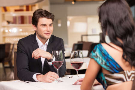 Seducing  handsome man looking at beautiful dark hair woman with wine glasses. Romantic and love moodの写真素材