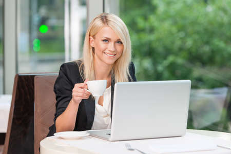 Smiling Blond business lady looking at camera. While sitting and drinking coffee or teaの写真素材