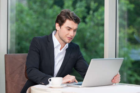 Handsome business man working on laptop. While drinking coffee and green nature on backgroundの写真素材