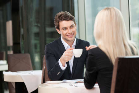 Smiling businessman drinking coffee. While talking to blond business womanの写真素材