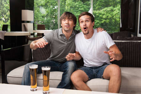 Two male football fans cheering football team. Drinking bear in pub, green trees on backgroundの写真素材