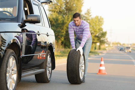Handsome young man rolling a spare wheel using glovesの写真素材